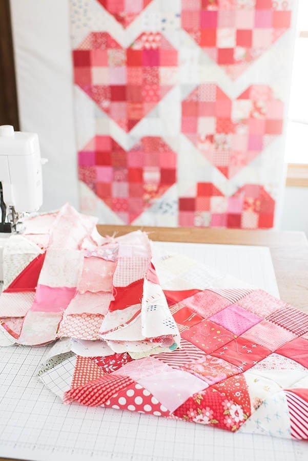 Scraps of heart quilt pattern fabric on cutting board near sewing machine.