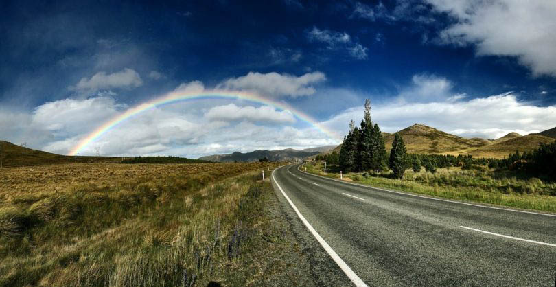 A highway horizon sits below a rainbow